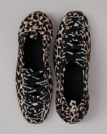 Top-down view of a pair of GANNI leopard-print ballerina flats with black lace-up detailing and metal eyelets, featuring printed text on the laces and elasticated heels on a neutral background.