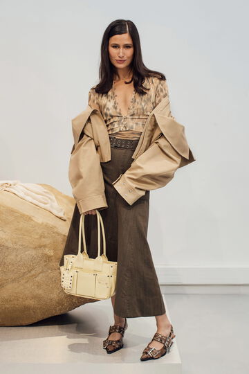 Model wearing a beige jacket and brown skirt carrying a yellow handbag