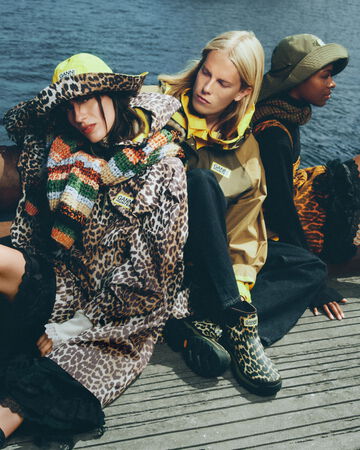 Models sitting on a dock by the water wearing GANNI x Hunter