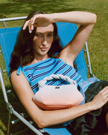 Model sitting on garden chair wearing blue, striped top and a GANNI Bou bag