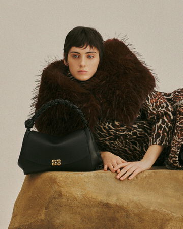 Model lying on a sofa wearing a patterned outfit with a large fur collar and black bag