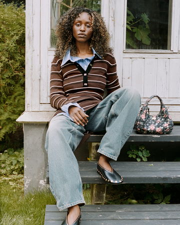 Model wearing sitting on staircase, wearing striped polo shirt and jeans