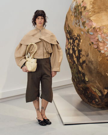 Model wearing beige cropped jacket and brown culottes holding a small handbag