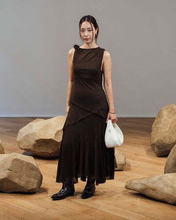 Model wearing brown draped dress holding a white handbag