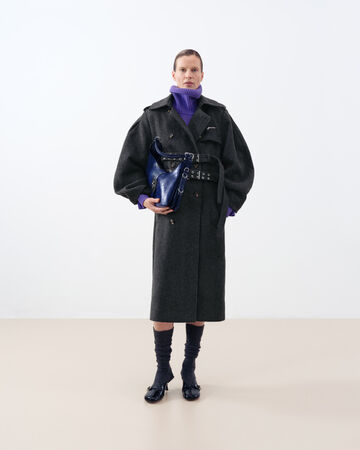 Model in long grey coat holding a blue bag