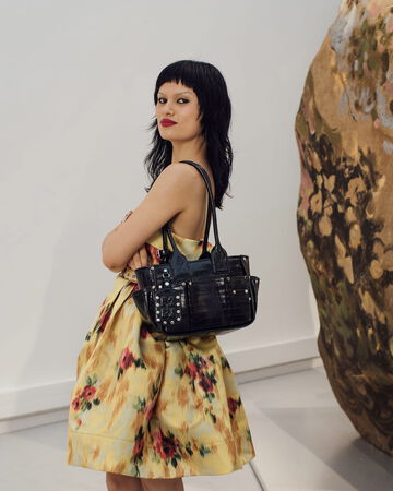 Model wearing a floral dress holding a black handbag