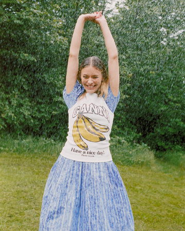 Model in garden, wearing white tank top with banana graphic and blue dress