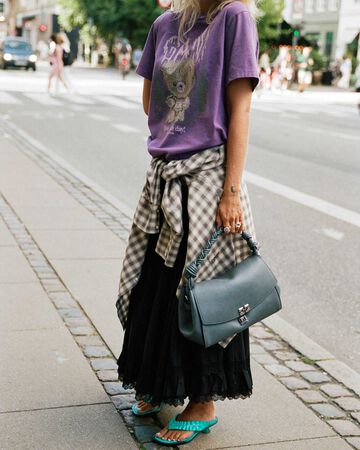Girl on the street wearing GANNI purple logo t-shirt and a black skirt, holding a grey Very Bou bag